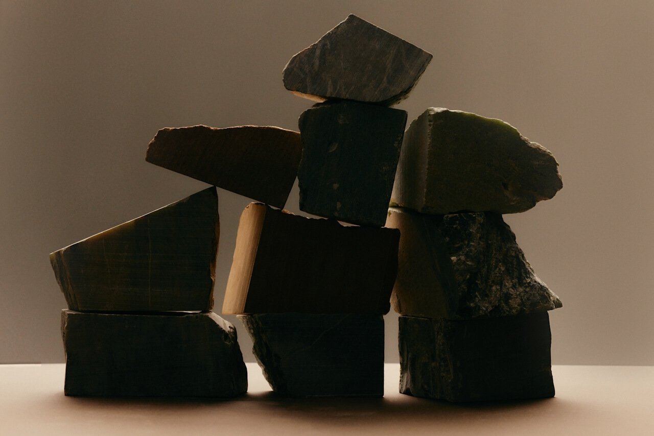 A stack of uneven, dark stone blocks balanced on each other against a plain, softly lit background.
