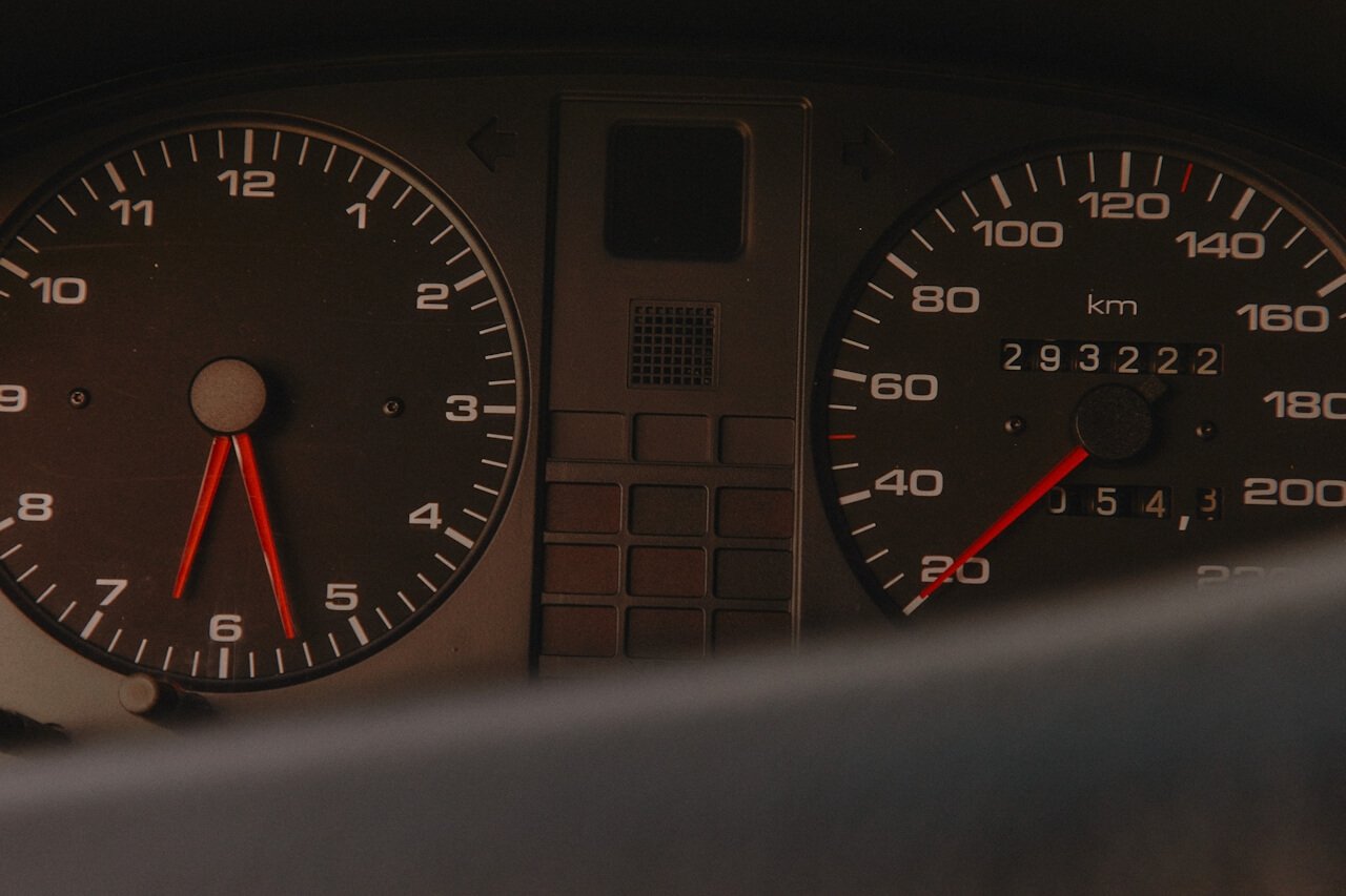 Close-up of a car dashboard showing a speedometer and tachometer. The speedometer reads about 130 km/h, the odometer shows 293222 kilometers, and part of the steering wheel is visible at the bottom.